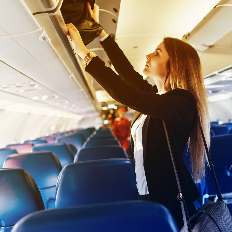  Frau, die ihre Tasche in das Handgepäckfach in einem Flugzeug legt
